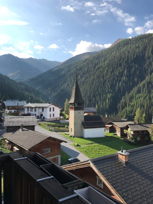 A village with traditional wooden houses, a church with a tall steeple, and a mountain backdrop.