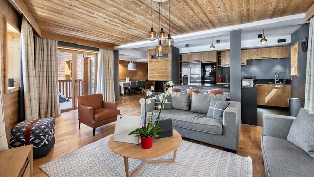 A spacious living room with a wooden ceiling, a sofa, a coffee table, and a dining area visible through an open door. - Prime Ski-In/Ski-Out Location, Modern 5-Room Apartment with Fireplace (Val-d'Isère)