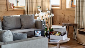 A modern living room with a grey sofa, a coffee table with a bottle of champagne, and a box of chocolates. - Prime Ski-In/Ski-Out Location, Modern 5-Room Apartment with Fireplace (Val-d'Isère)