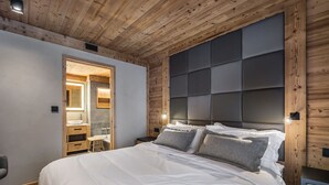 A bedroom with a wooden ceiling, a large bed with white bedding, a bedside table, and a built-in headboard. - Prime Ski-In/Ski-Out Location, Modern 5-Room Apartment with Fireplace (Val-d'Isère)