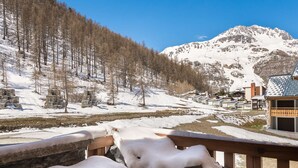 A snowy mountain landscape with a wooden deck and a building with a sloped roof. - Prime Ski-In/Ski-Out Location, Modern 5-Room Apartment with Fireplace (Val-d'Isère)