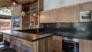 Une cuisine moderne avec des meubles en bois, un plan de travail noir, des appareils en acier inoxydable et des luminaires suspendus.