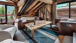 Une pièce chaleureuse aux hauts plafonds, avec un plafond en bois, des canapés en cuir, une table basse en bois et de grandes fenêtres donnant sur l’extérieur.