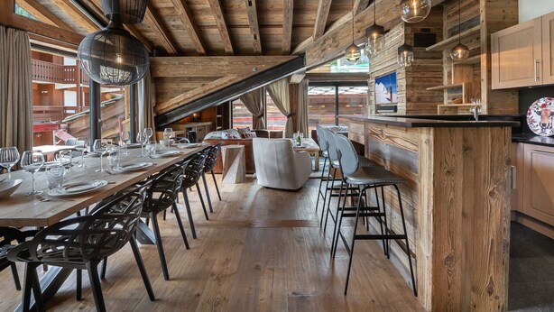 Un coin repas rustique avec des poutres en bois, une longue table dressée et des lampes suspendues.