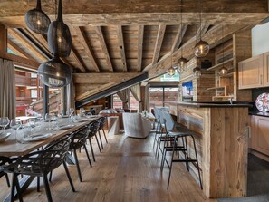 A rustic dining area with wooden beams, a long table set for dining, and hanging pendant lights.