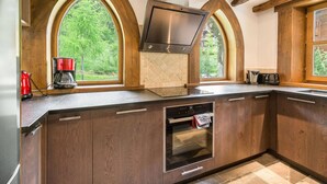 A kitchen with wooden cabinets, a built-in oven, a coffee maker, and a large window with a view of greenery.
