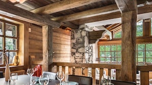 A dining area with a stone wall, wooden beams, and a view of greenery outside.