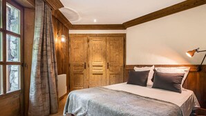 A bedroom with a wooden bed, a large window with curtains, and a wooden ceiling.
