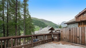 A wooden deck with a railing, overlooking a mountainous landscape with buildings in the background.