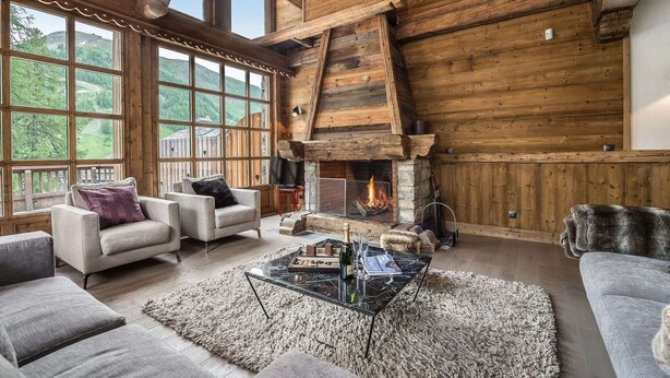 A cozy log cabin interior with a fireplace, large windows, and comfortable seating.