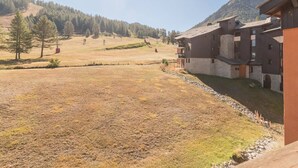 A mountain lodge with a stone facade, multiple balconies, and a view of a forested hillside. - Apartment Montgenèvre 4 people, parking, ski-in/ski-out (Montgenèvre)