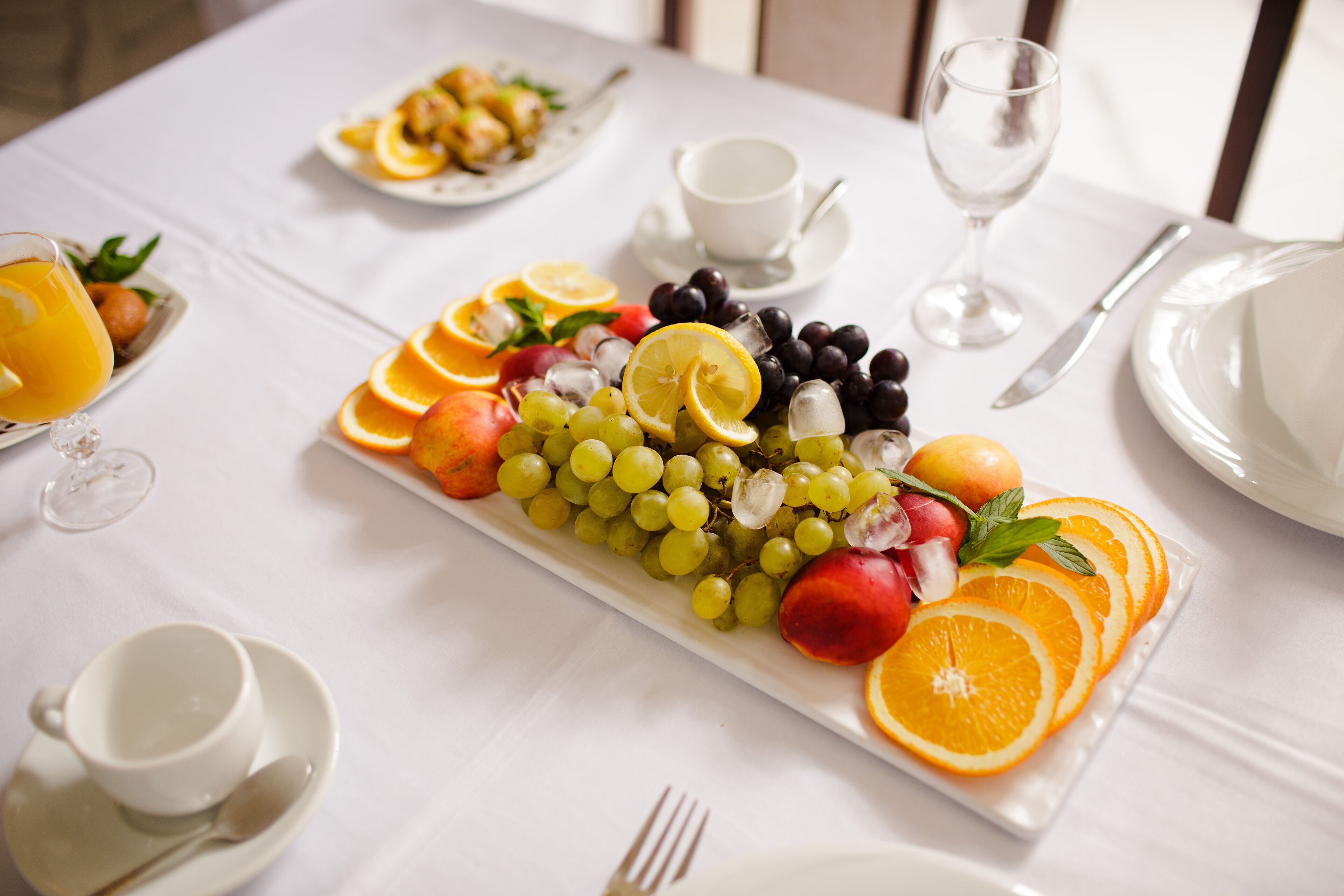 A breakfast setting with a fruit platter, a glass of orange juice, and a cup of coffee on a white tablecloth.