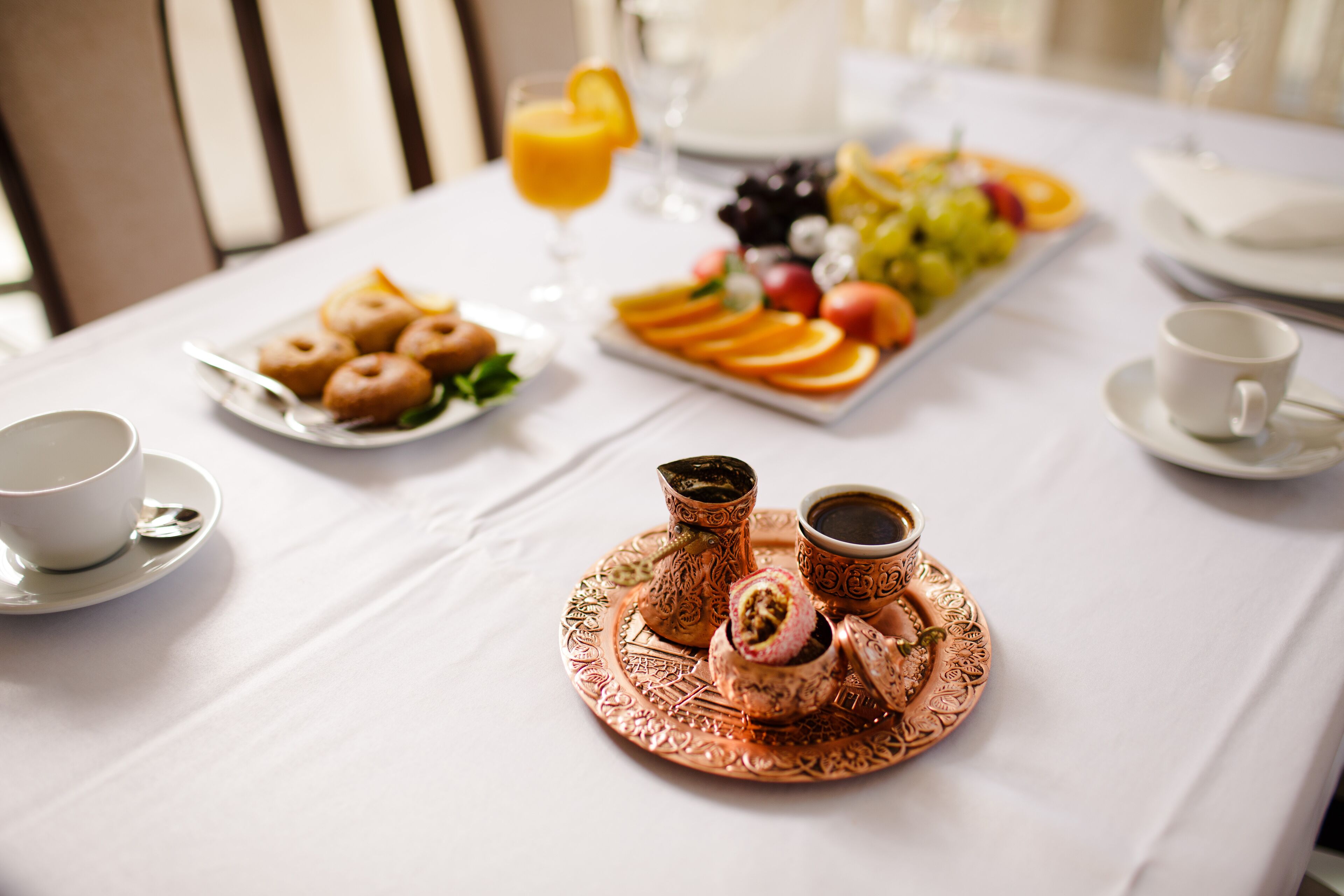 A breakfast setting with a tray of pastries, fruits, and coffee on a white tablecloth.