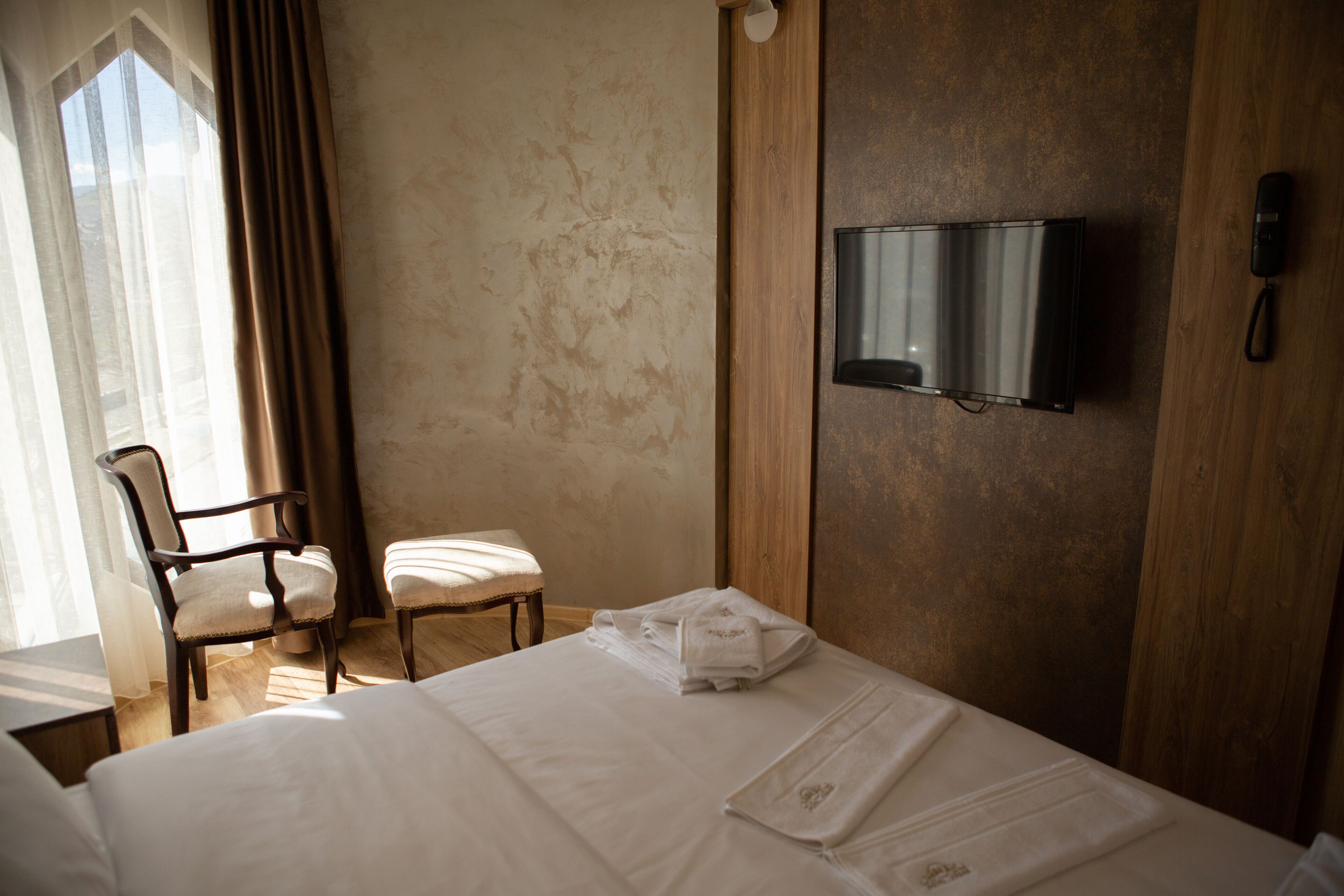 A hotel room with a bed, a chair, a television mounted on the wall, and a telephone.