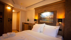Habitación de hotel con una cama grande, cabecera de madera, un cuadro sobre la cama y un escritorio con lámpara.