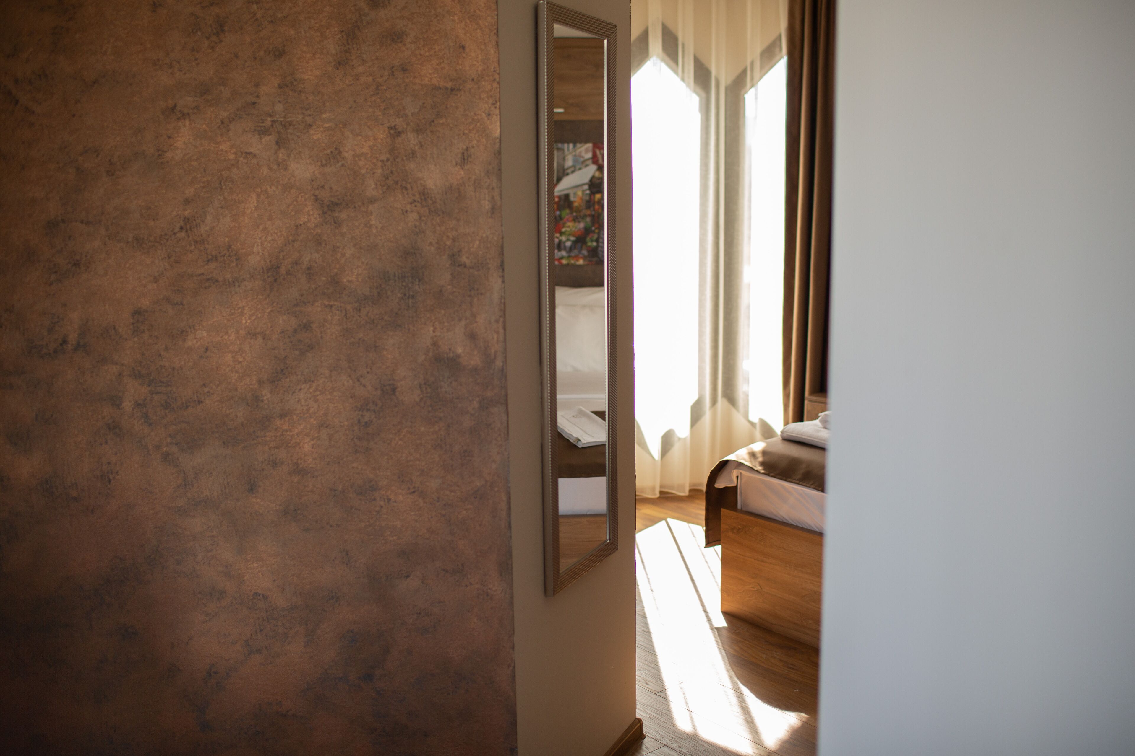 Una habitación con pared texturizada, una cama con cabecera de madera y una ventana con cortinas.