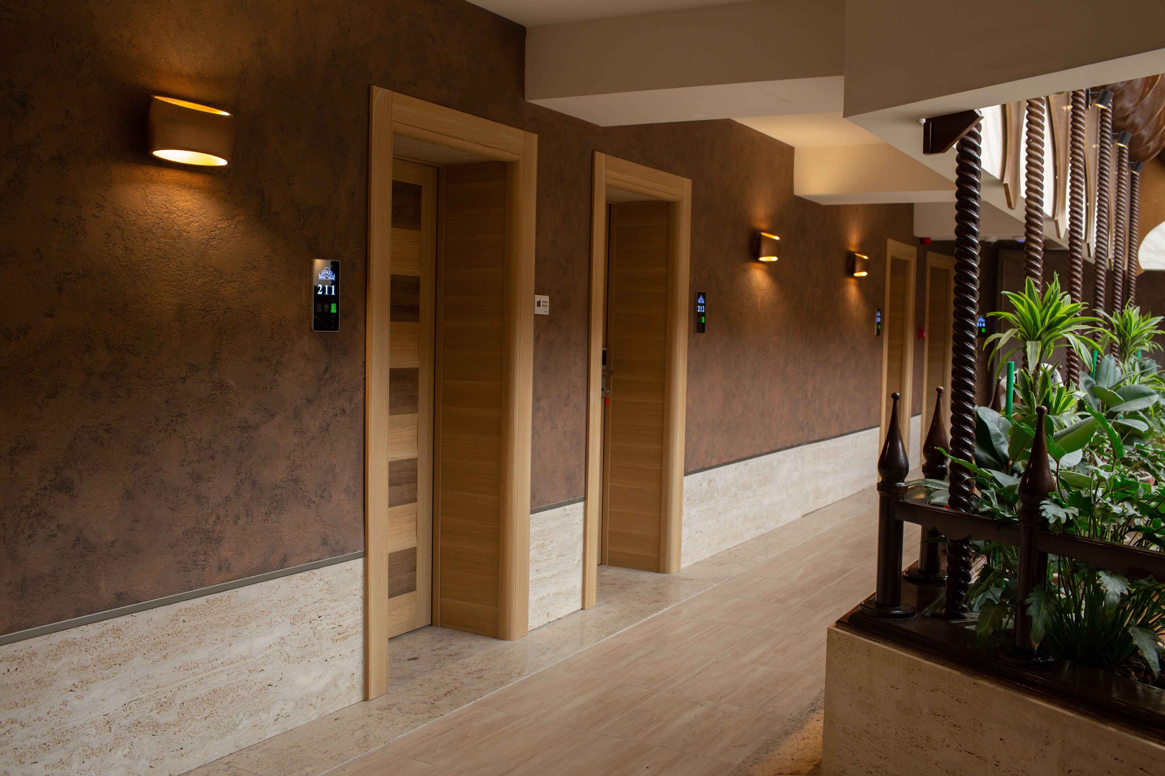 A hallway with wooden doors, a digital elevator display, and a plant arrangement.