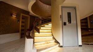 Una escalera en espiral con barandilla, una puerta en la parte superior y una lámpara en la pared.