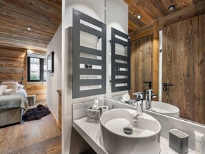 Een moderne badkamer met een grote spiegel, een wastafel en een houten plafond.