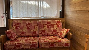 A wooden cabin interior with a sofa featuring a red and white checkered pattern, a window with a sheer curtain, and a wooden wall. - Ground floor studio with terrace, garden and parking, Montgenèvre (Montgenèvre)