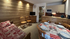 A cozy room with a wooden wall, a sofa, a dining table set for four, and a kitchenette with a microwave. - Ground floor studio with terrace, garden and parking, Montgenèvre (Montgenèvre)