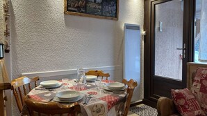 A dining area with a table set for four, a wooden chair with a cushion, a wall-mounted picture, and a door with a frosted glass panel. - Ground floor studio with terrace, garden and parking, Montgenèvre (Montgenèvre)