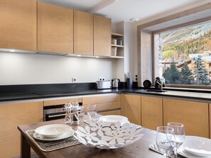 A modern kitchen with wooden cabinets, a black countertop, and a dining area set for four. - Modern Duplex Apartment, Ski Shuttle, Parking, Pet-Friendly (Val-d'Isère)