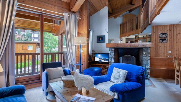Een gezellige woonkamer met blauwe banken, een houten salontafel en een open haard.