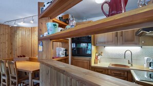 Een houten keuken met een eettafel en stoelen, een koffiezetapparaat en een rode mok op de plank.