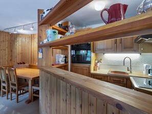 Eine Holzküche mit Esstisch und Stühlen, einer Kaffeemaschine und einer roten Tasse auf dem Regal.