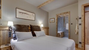 A bedroom with a large bed, wooden headboard, two bedside lamps, a framed picture on the wall, and a wooden door.