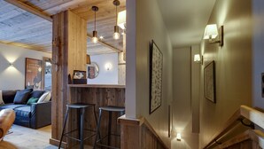 A cozy interior with a wooden staircase, a bar area, and a seating area with a sofa and stools.