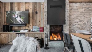 A cozy living room with a stone fireplace, wooden panel walls, a television, and a fur rug. - Luxurious 4-Bedroom Apartment in Val d'Isère with Hammam, Fireplace, and Balconies (Val-d'Isère)