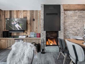 Una sala de estar acogedora con una chimenea de piedra, paneles de madera y una alfombra de piel, además de un televisor.
