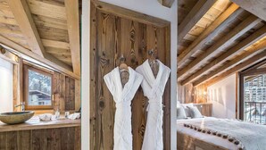 A wooden cabin interior with a wooden-framed bed, a wooden vanity with a bowl sink, and two white robes hanging on a wooden door. - Luxurious 4-Bedroom Apartment in Val d'Isère with Hammam, Fireplace, and Balconies (Val-d'Isère)