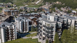 Une ville de montagne où se côtoient des bâtiments modernes et traditionnels, notamment des immeubles à plusieurs étages dotés de balcons et un bâtiment central surmonté d’un toit en pente.