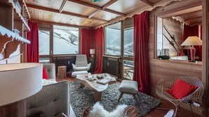 Une pièce chaleureuse avec un plafond en bois, de grandes fenêtres ornées de rideaux rouges, une cheminée et un coin salon confortable.
