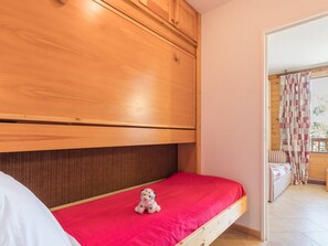 Quarto com cama beliche de madeira, colchão vermelho e um pequeno brinquedo de pelúcia na cama inferior.