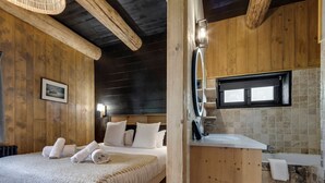 A wooden-themed bedroom with a bed, towels, a headboard, a bedside lamp, and a framed picture on the wall.