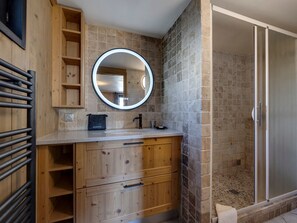 Une salle de bain avec un meuble-lavabo en bois, un miroir rond, une douche aux carreaux de pierre et un porte-serviettes.