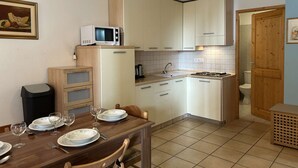 Una cocina compacta equipada con microondas, fregadero y estufa. Hay una mesa de comedor con platos y vasos.