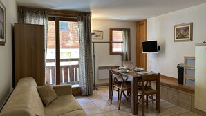 Una sala de estar acogedora con un sofá, una mesa de comedor preparada para cuatro personas y un televisor montado en la pared.