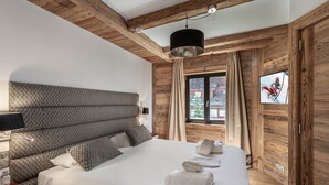 Ein Schlafzimmer mit einem großen Bett, Holzbalken, einem Fernseher und einem Fenster mit Vorhängen.