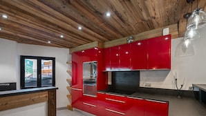 Eine moderne Küche mit roten Schränken, einem Edelstahlkühlschrank und einer Holzbalkendecke.