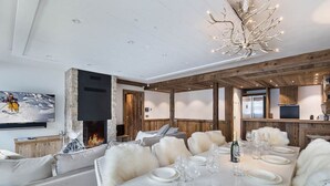 Un salon moderne avec une cheminée, un coin repas aménagé pour six personnes et une cuisine agrémentée d'éléments en bois.