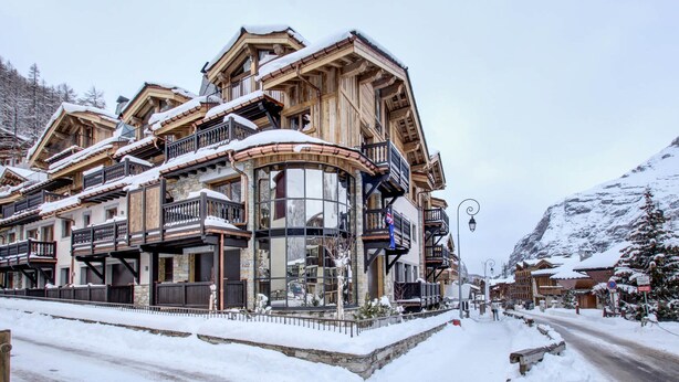 Un bâtiment traditionnel en bois, doté de nombreux balcons et d’une partie en verre incurvée, entouré de neige.