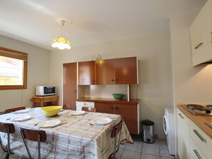 Cozinha compacta com mesa de jantar posta para quatro pessoas, micro-ondas, armários de madeira e máquina de lavar.