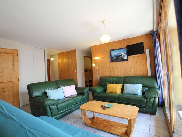 Ein Wohnzimmer mit zwei grünen Ledersofas, einem Holztisch und einem an der Wand montierten Fernseher.