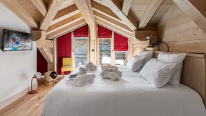 A cozy bedroom with a large bed, wooden beams, a TV, and a window with red curtains. - Spacious chalet near slopes with sauna and WiFi, pets allowed (Val-d'Isère)