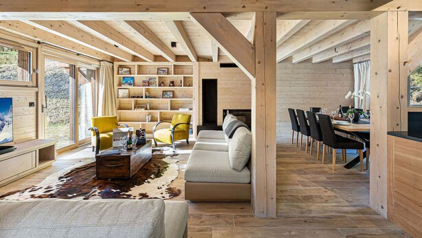 A spacious living area with a sofa, chairs, a wooden bookshelf, and a dining table with chairs. - Spacious chalet near slopes with sauna and WiFi, pets allowed (Val-d'Isère)
